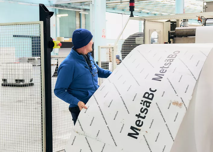Man handling large sheet of paperboard in factory